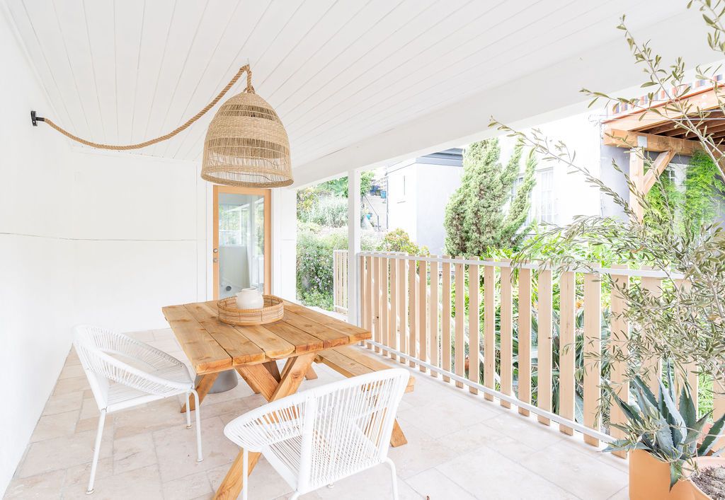 Ein Picknicktisch aus hellem Holz und weiße Stühle auf einer Veranda