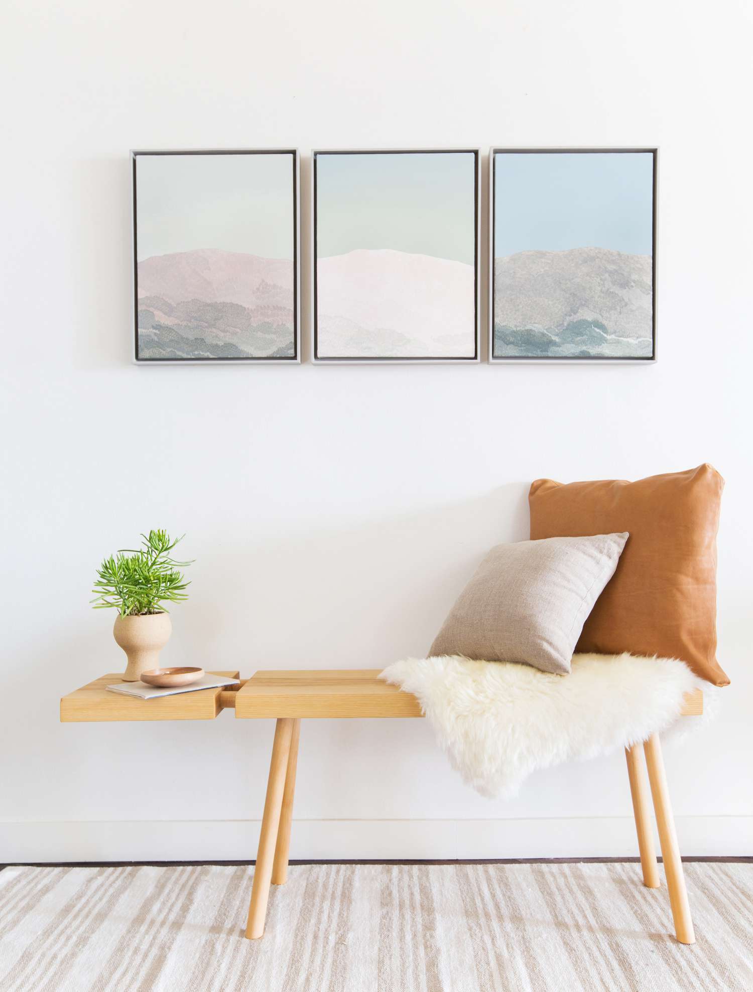 A simple wood bench is cozied up with a faux fur blanket and three hanging wall art pieces capturing images of mountain tops