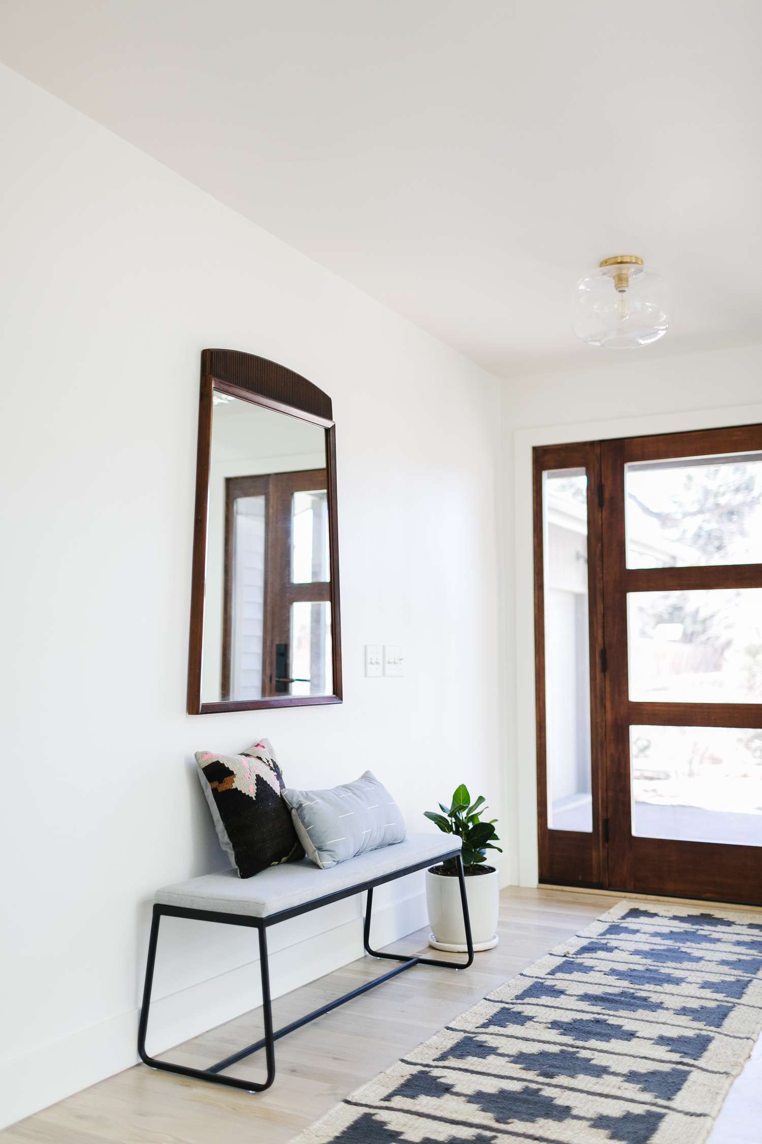 A white entryway wall has a Midcentury Modern style mirror in wood matching the front door.