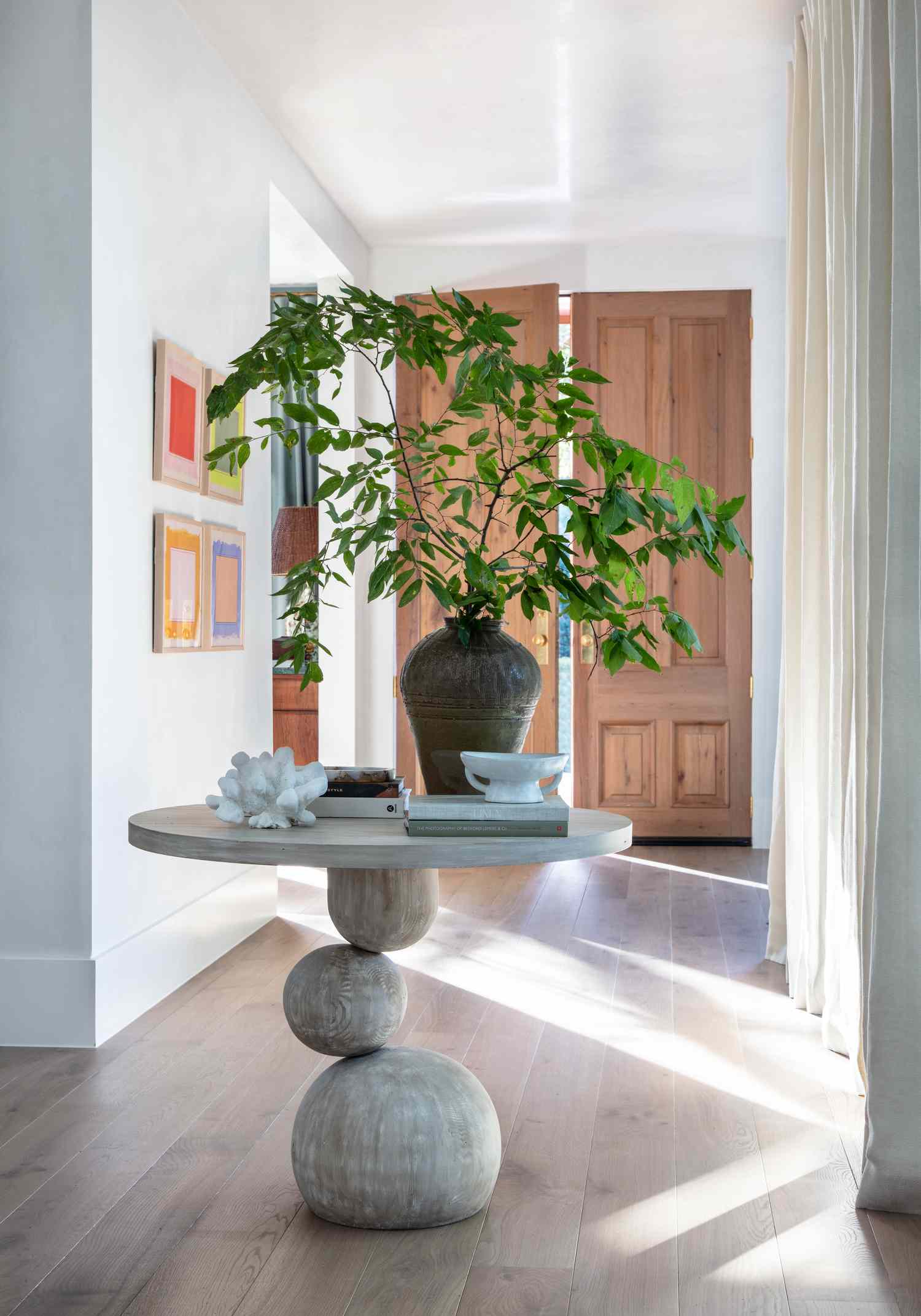 Large wooden doors open to a modern entryway table paired with four brightly colored framed artworks in neon water colors.