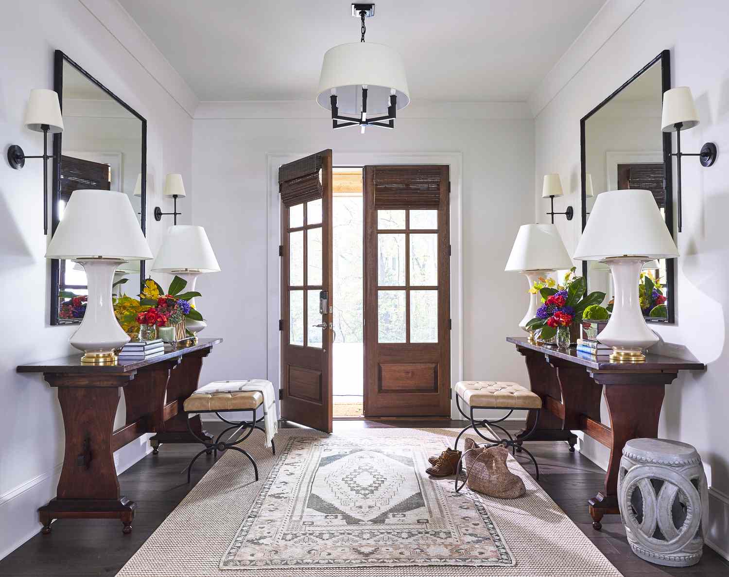 Two entryway walls have identical side tables covered in two lamps and potted flowers