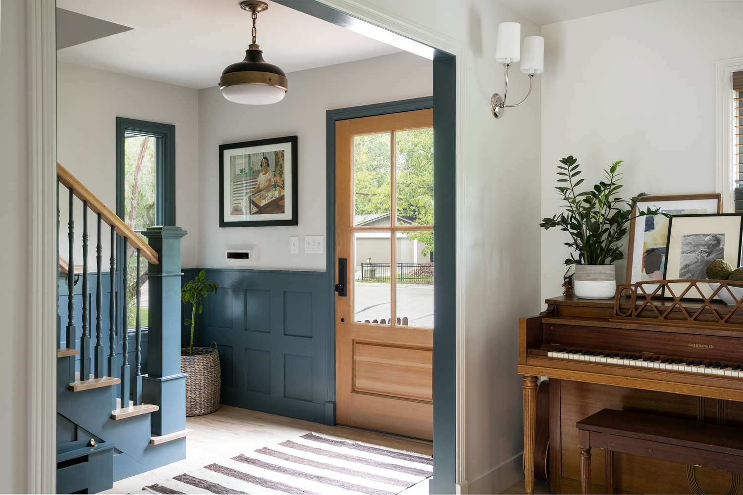 An entryway wall is decorated to match another nearby wall. Both are outfitted with art deco style mirrors and semi circle shaped side tables on which sit white lamps and a houseplant.