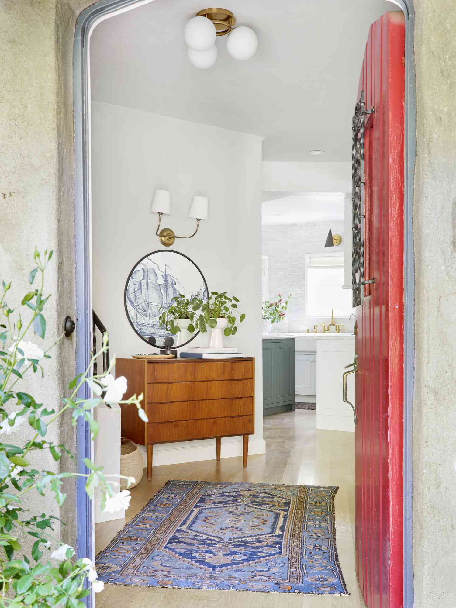 An entryway has a bright blue rug along with a nightstand upcycled into a small side table covered in houseplants.