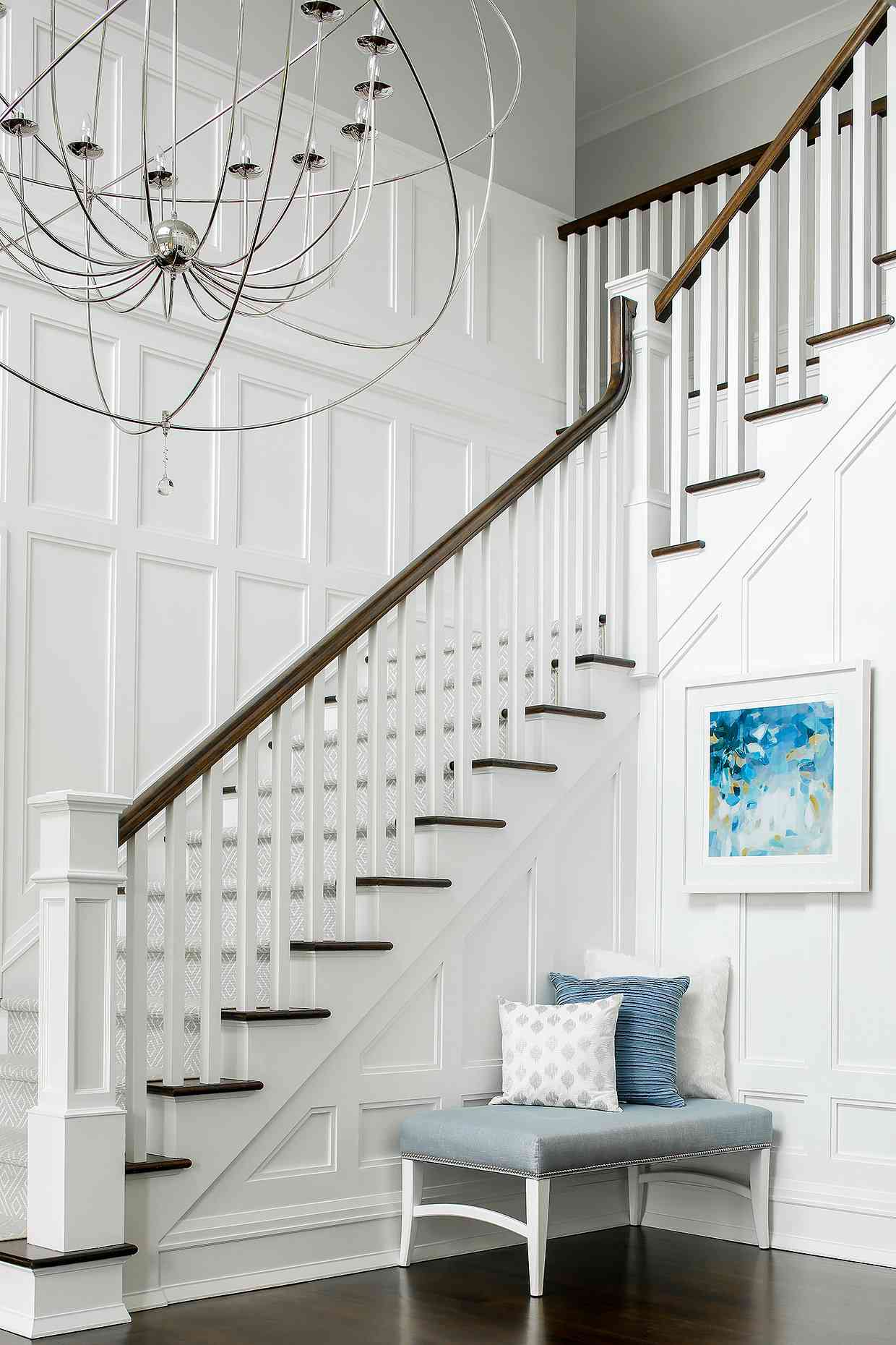 An entryway wall has decorative paneling in white and a white framed blue piece of artwork is hung above the paneling