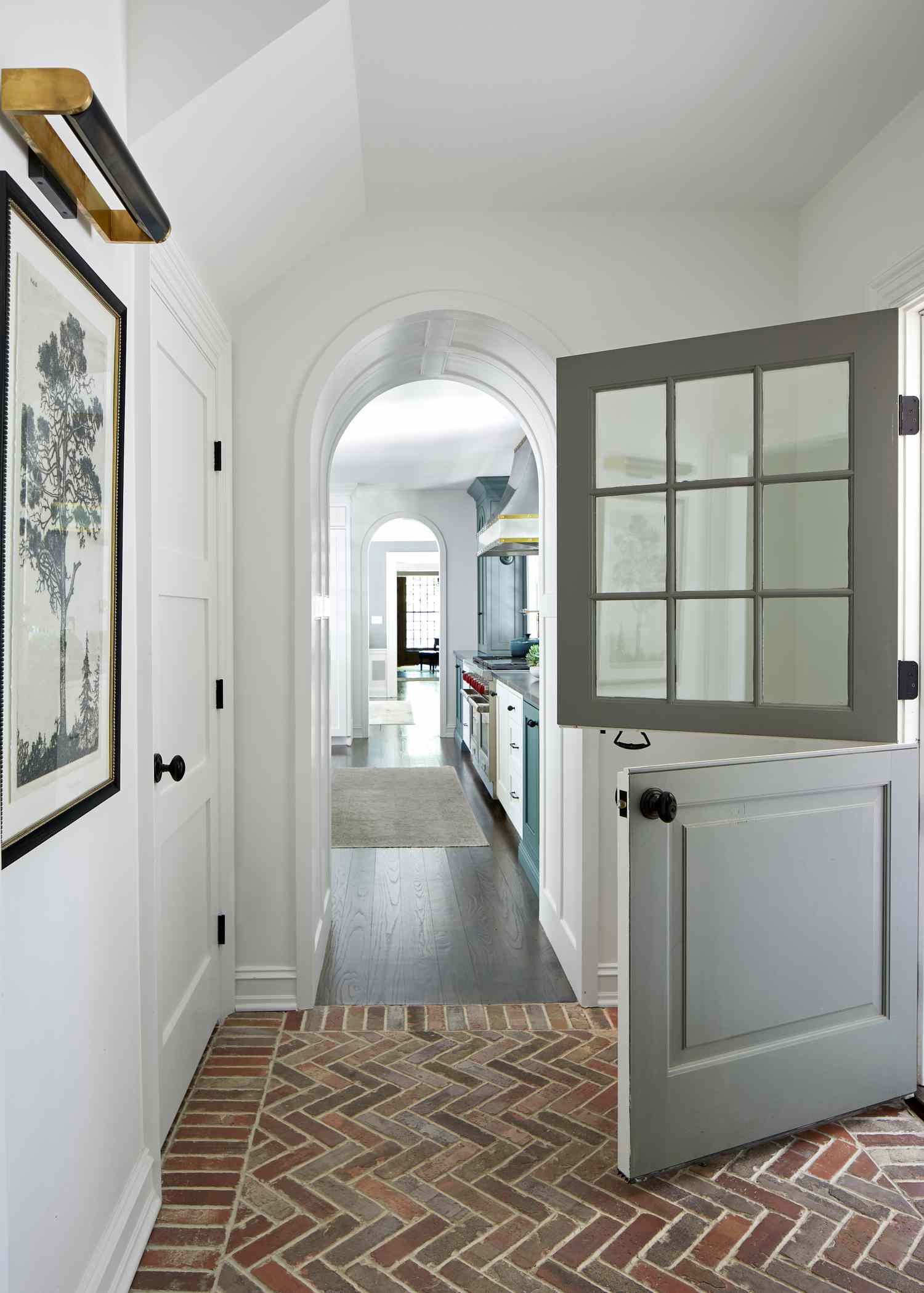 A farmhouse style door opens to a brick entryway that leads to a framed drawing of a tree 