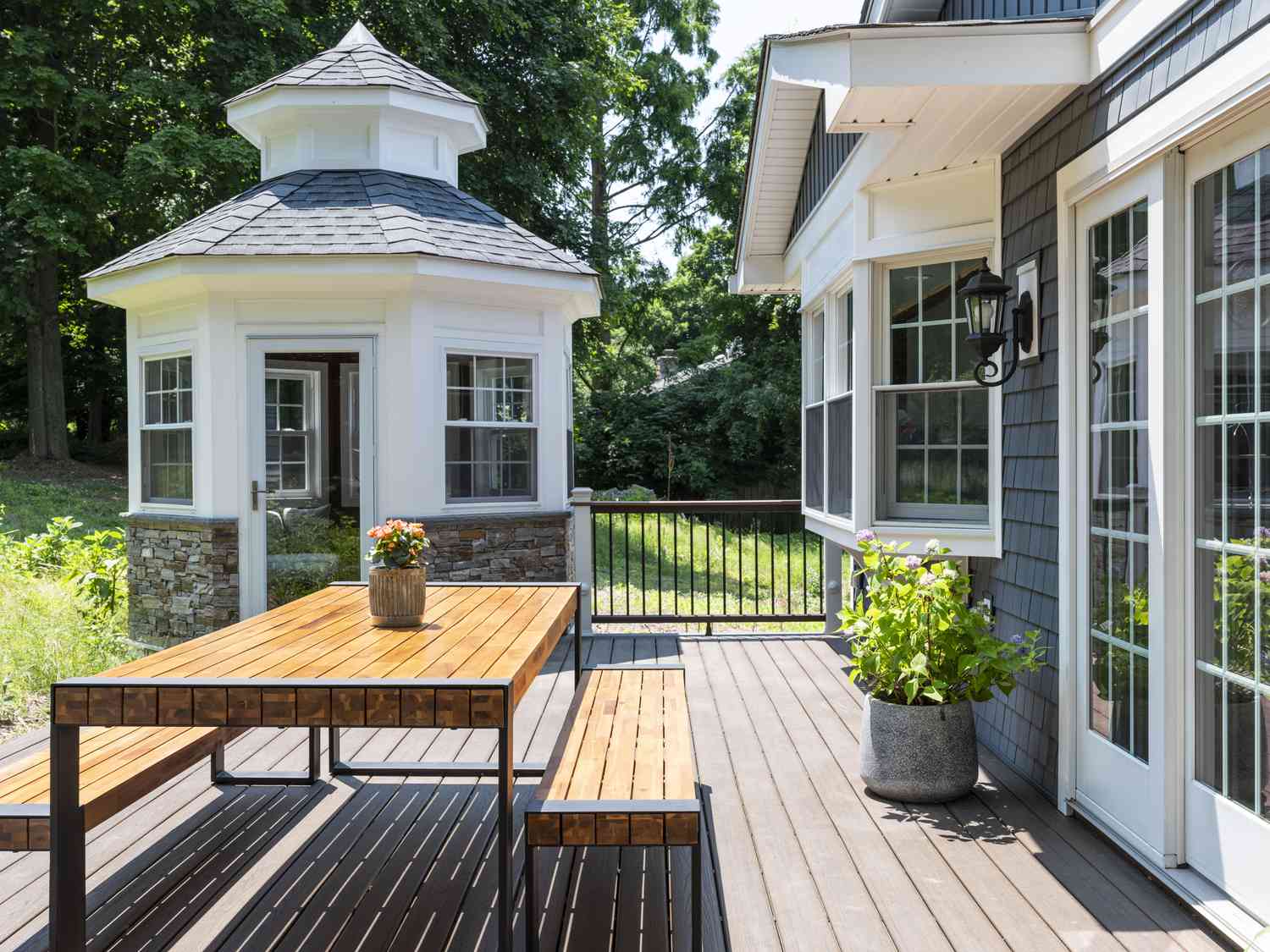 Eine Terrasse mit einer hölzernen Essbank außerhalb eines blau-grauen Hauses und dem weißen Wintergarten