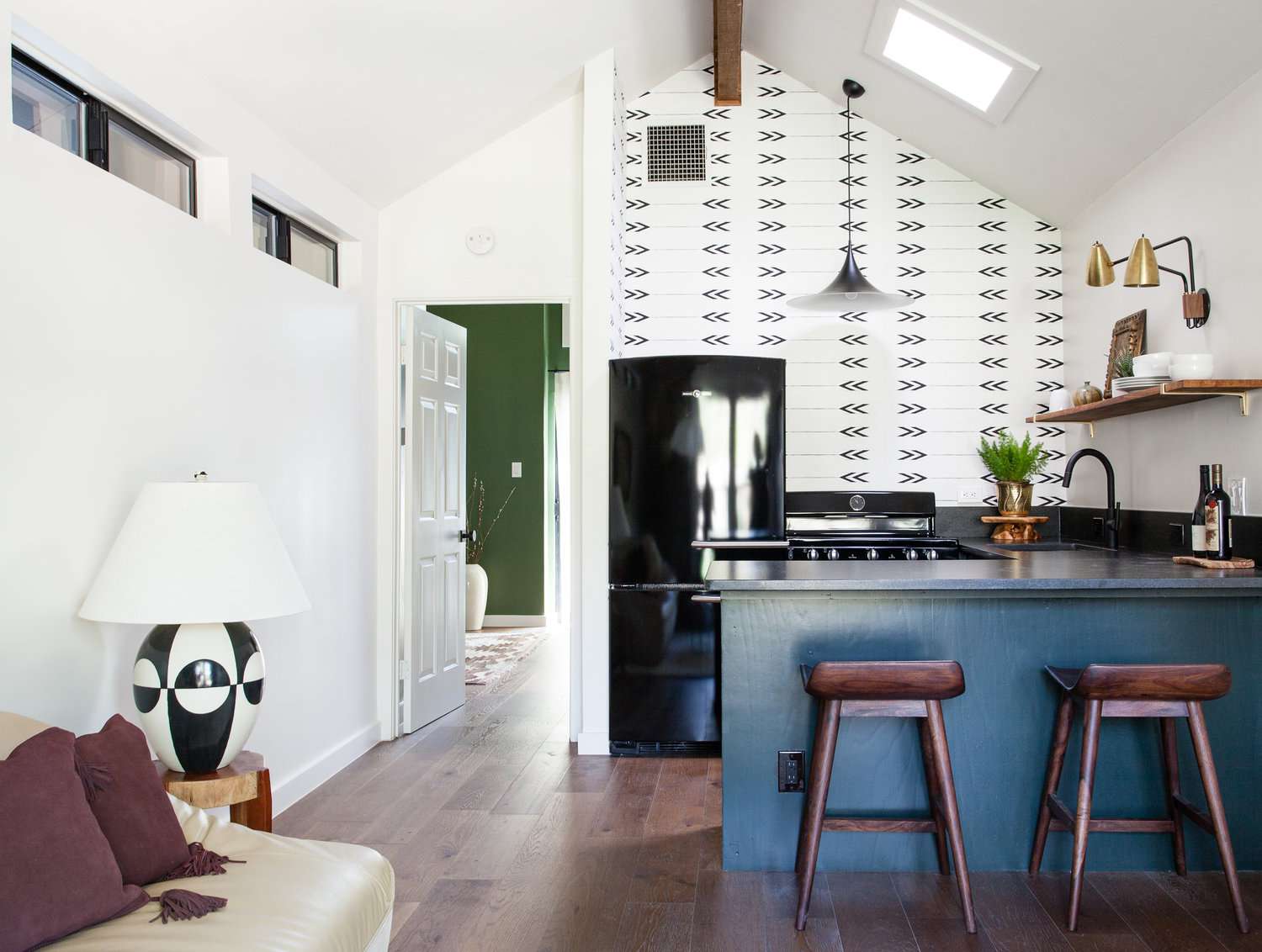 Kitchen with graphic wallpaper and blue painted lower cabinets opened to living room