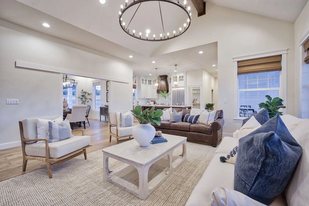 Open living room with large wagon wheel chandelier and kitchen in the background