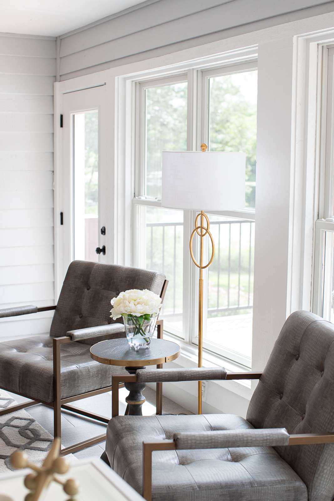 Modern furniture and a white and gold floor lamp in a small sunroom with light gray walls