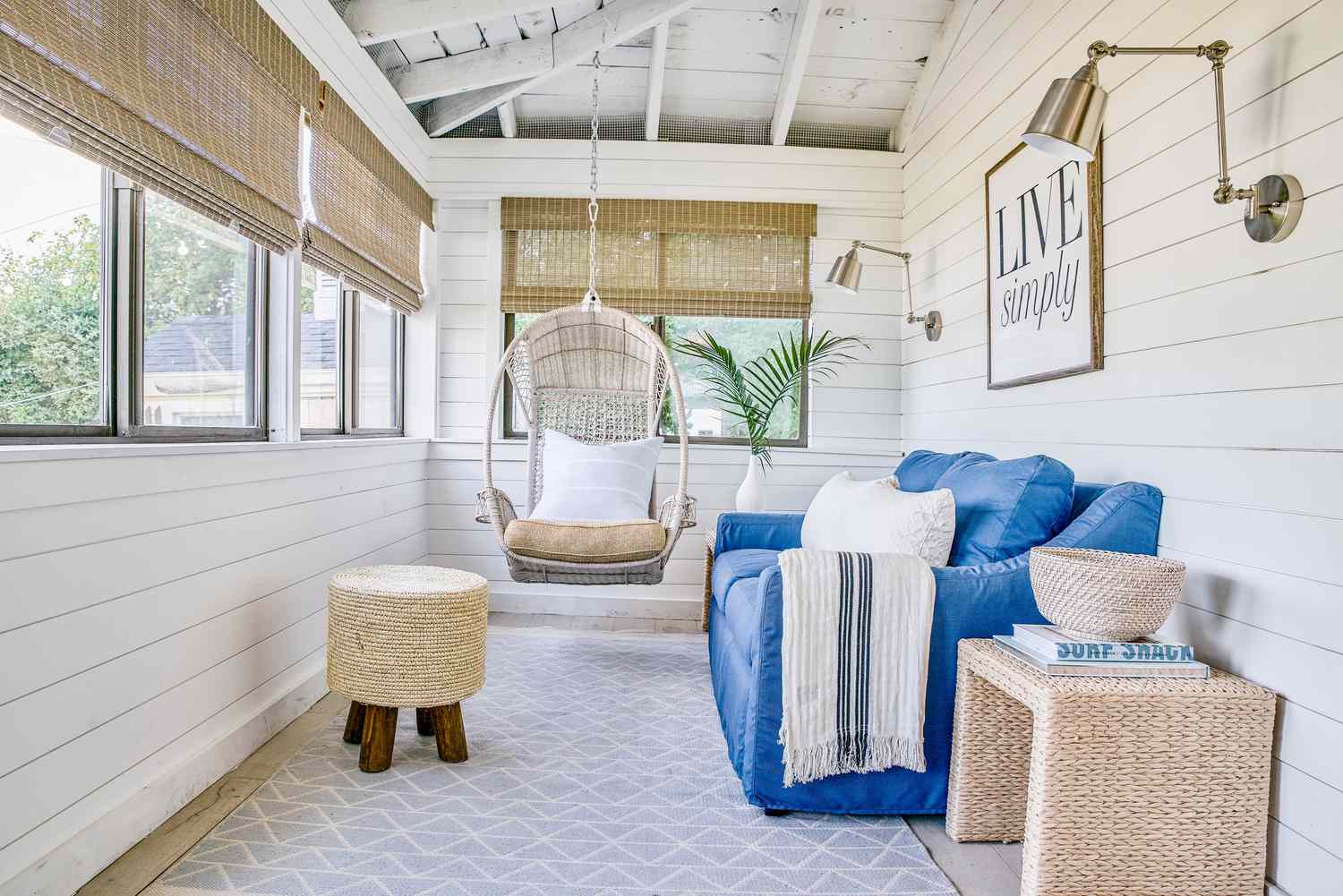 Sunroom with white shiplap walls, blue sofa, rattan window shades and a hanging chair