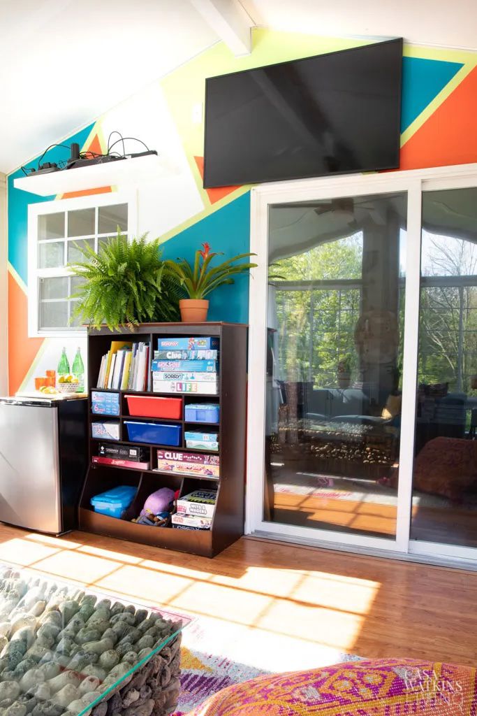 Color blocked sunroom wall and a TV mounted on the wall and a bookshelf with board games underneath it