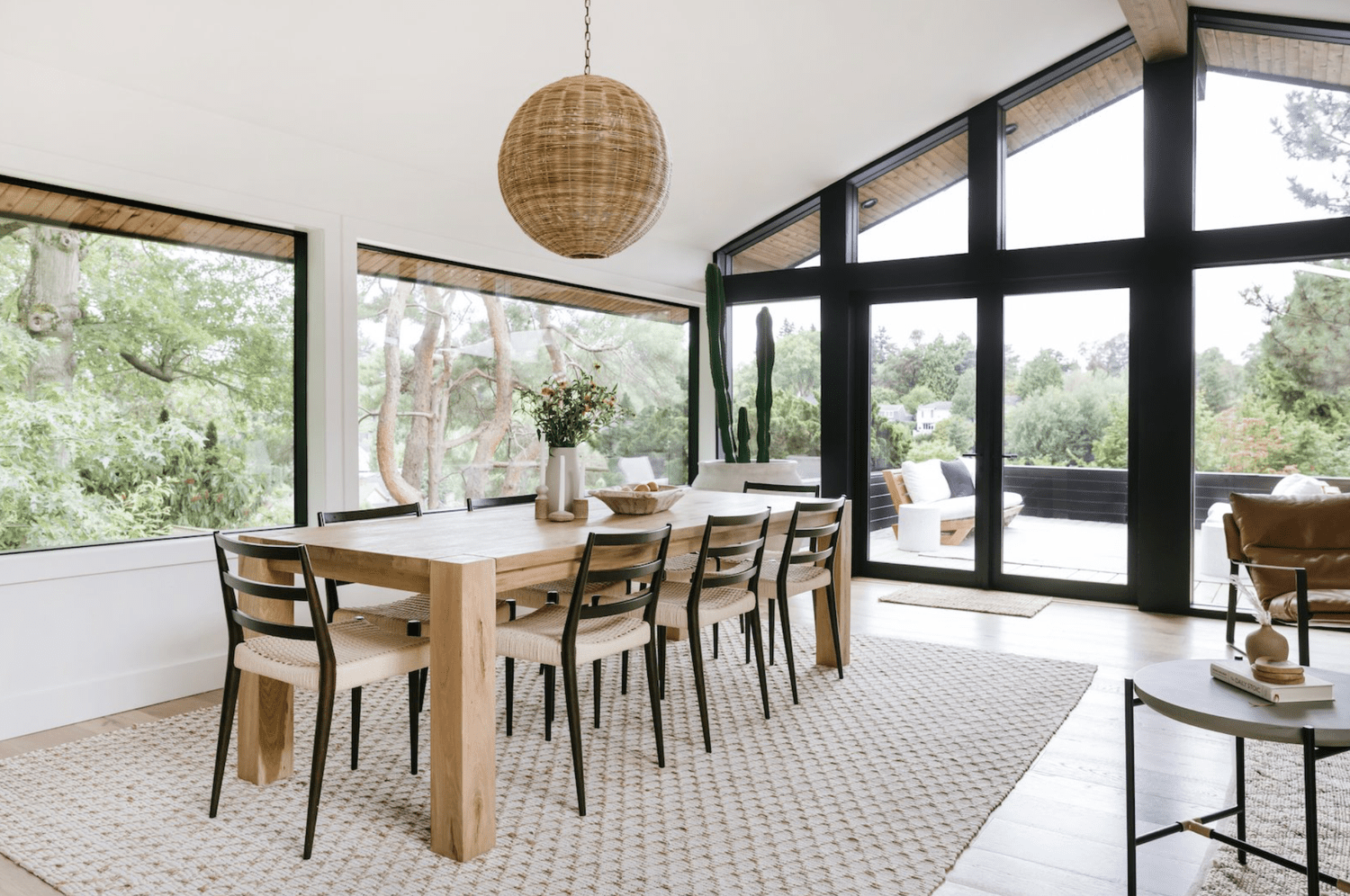 Sunroom with white walls, black window frames, wood furniture and rattan pendant light