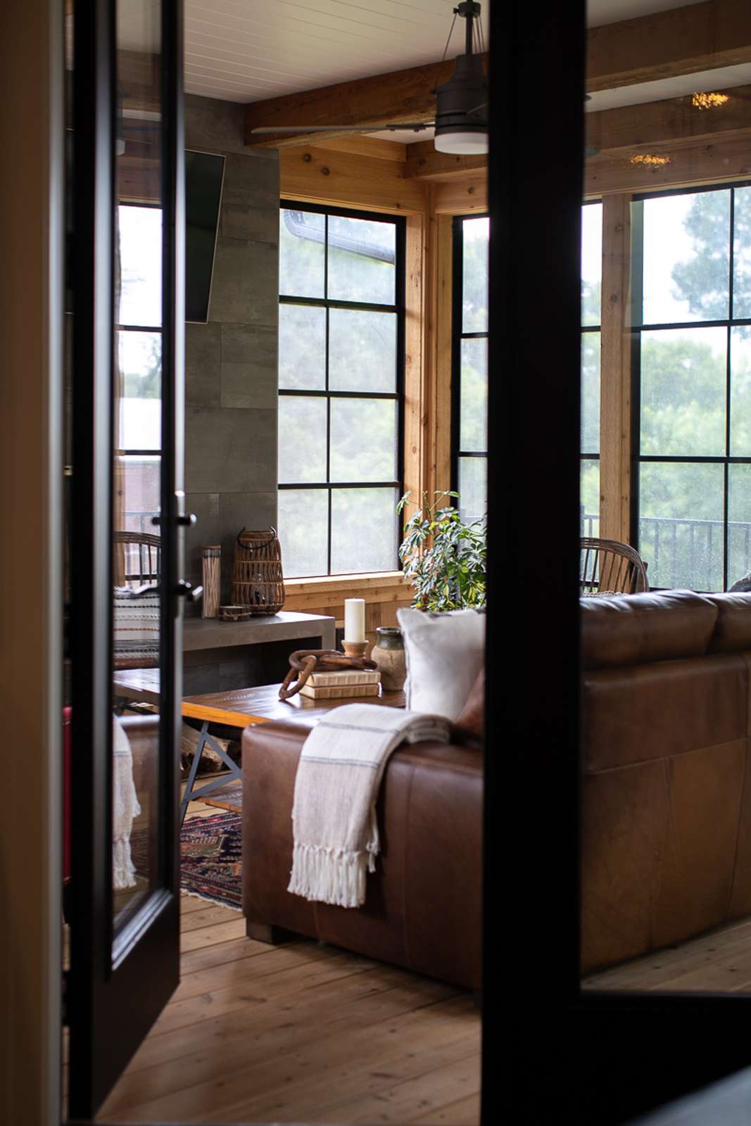 Modern rustic sunroom with wood walls, stone fireplace, and leather furniture