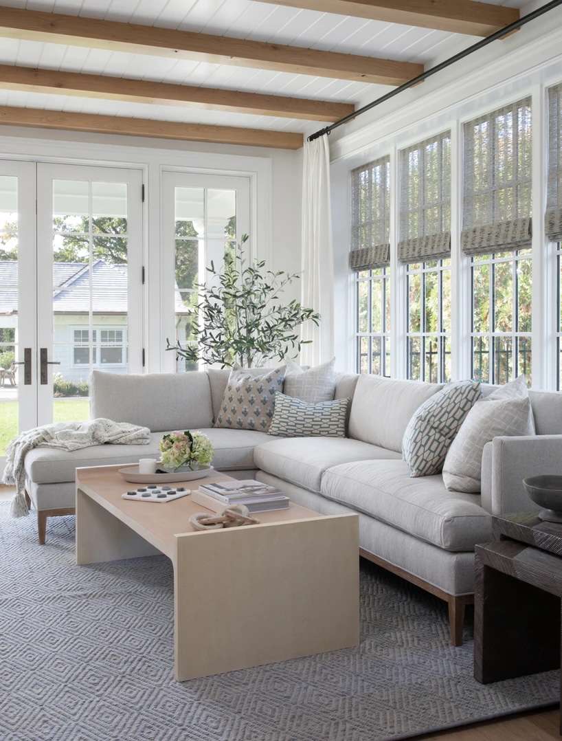 White sunroom with wood ceiling beams and a light gray sectional