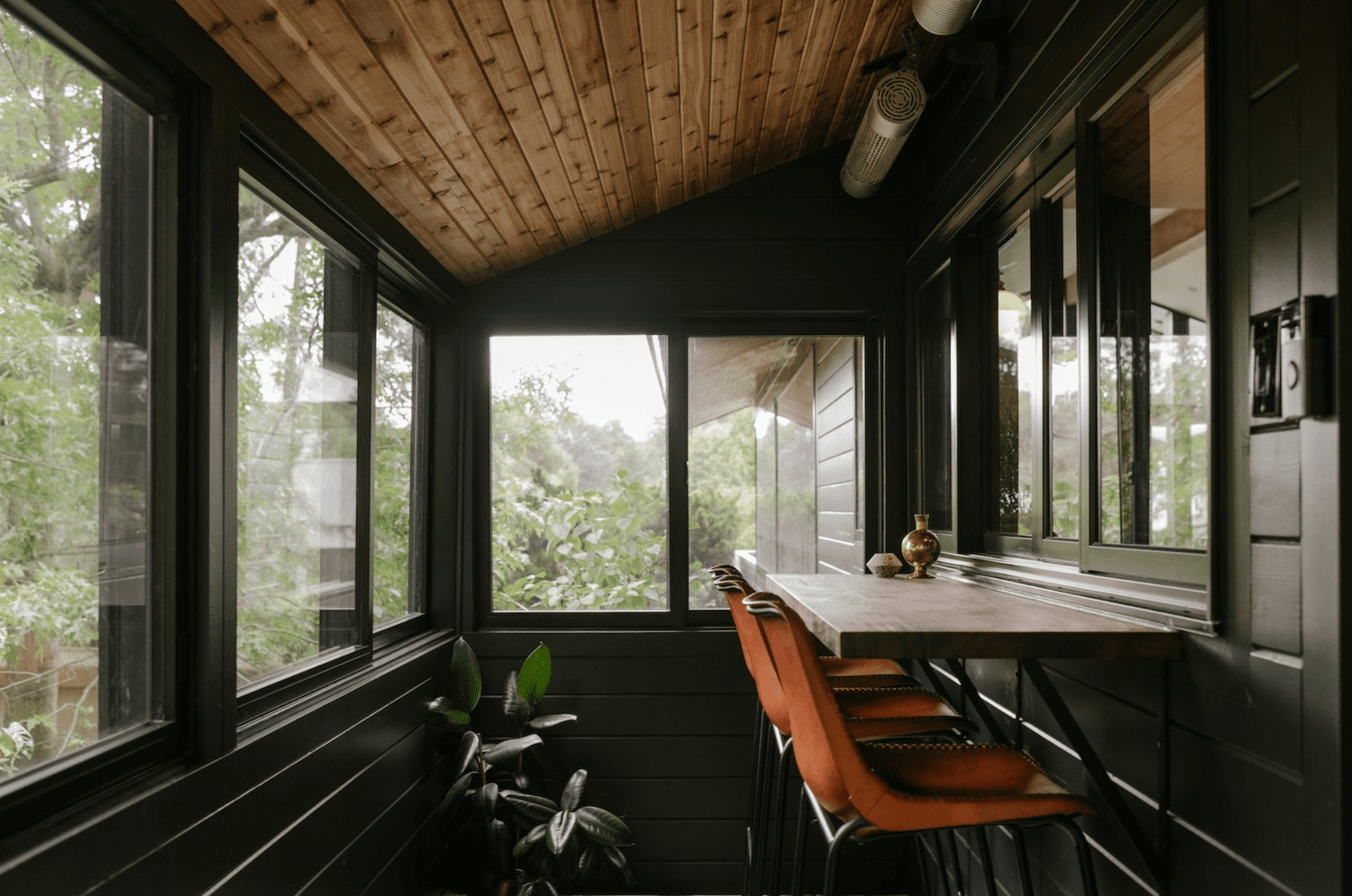 Small sunroom with black walls, wood ceiling and built-in counter with leather bar stools