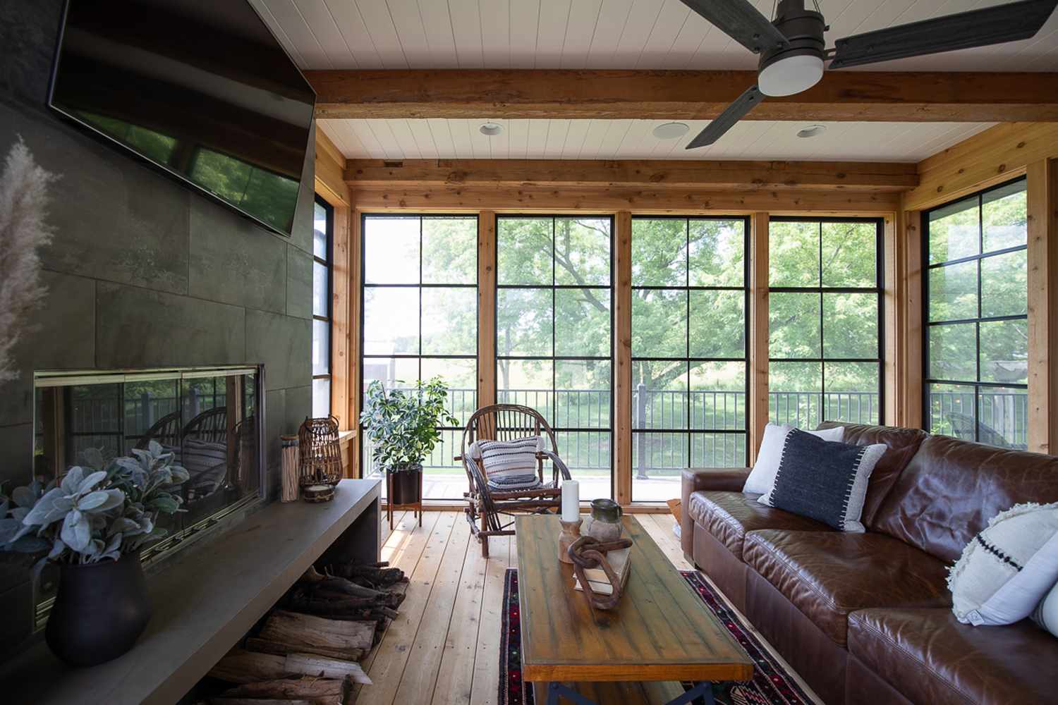 Sunroom with wood walls and flooring and a stone fireplace with a TV mounted above it