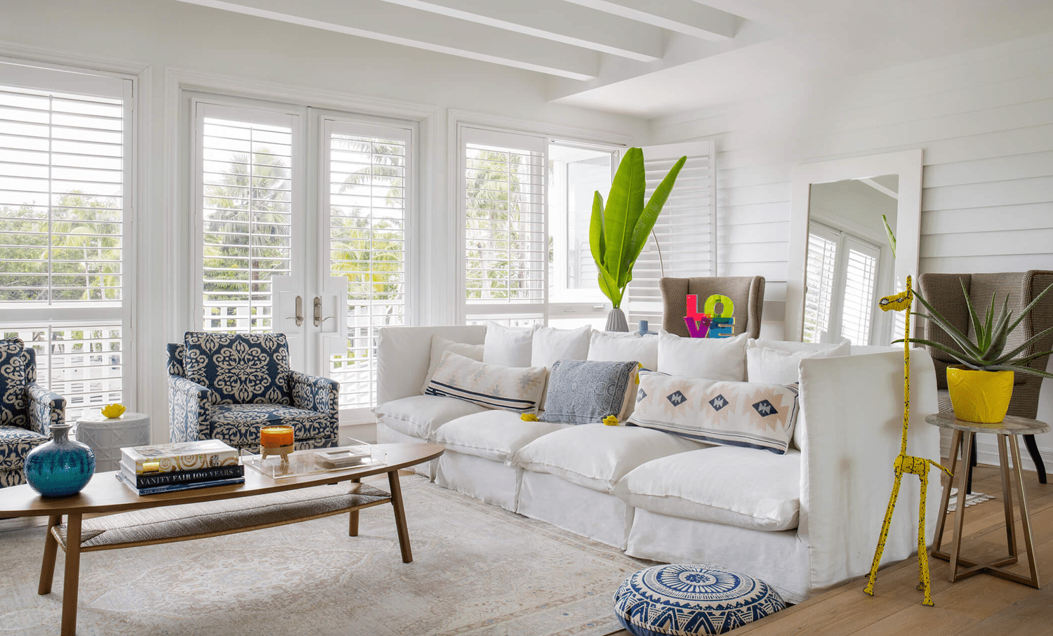 White sunroom with a big white sofa, patterned armchairs, wood coffee table and accessories