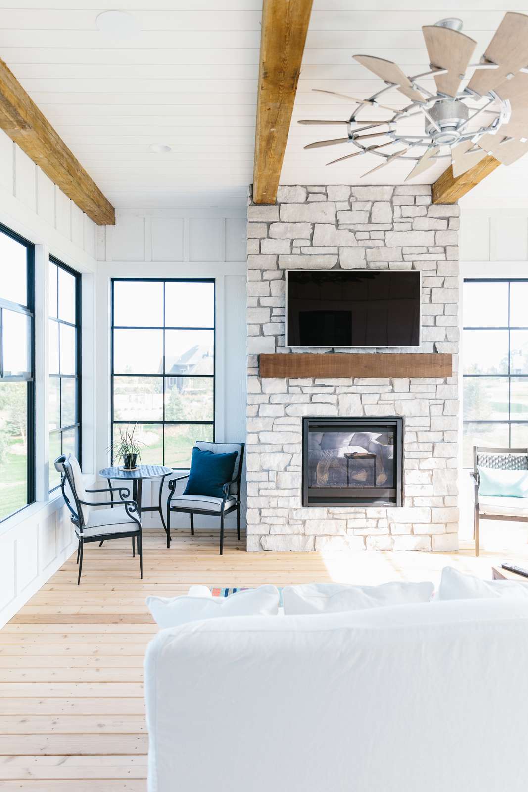 Sunroom with wood ceiling beams and a stone fireplace accent wall with a TV mounted above the mantel