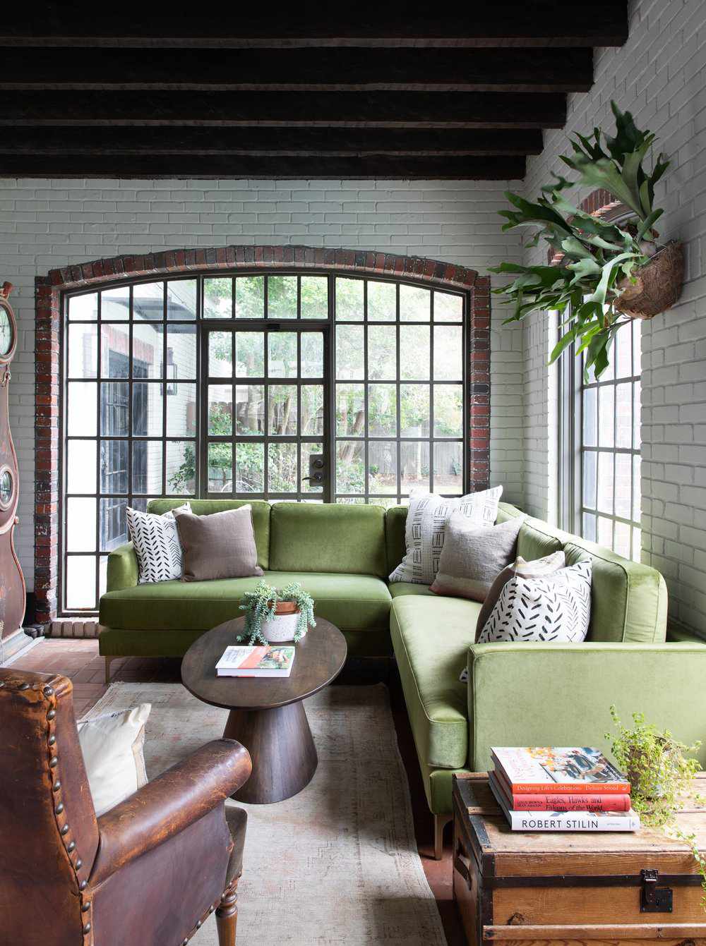 Sunroom with white painted brick walls, wood ceiling beams and a green sectional