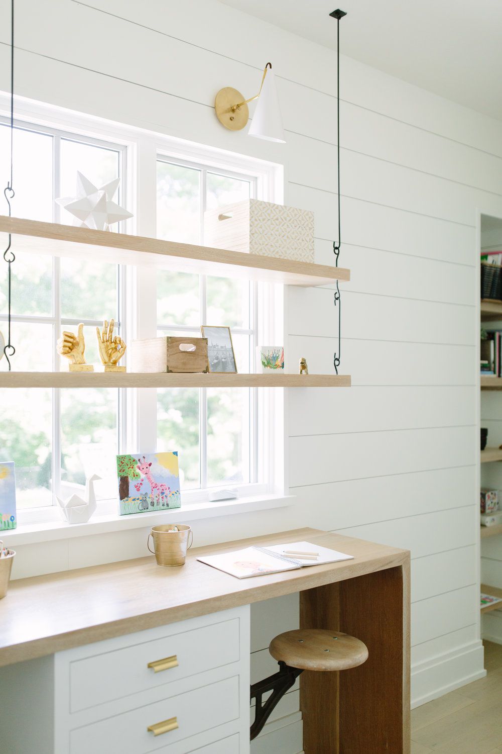 Hanging shelves in front of a window and above a wood desk in a white sunroom