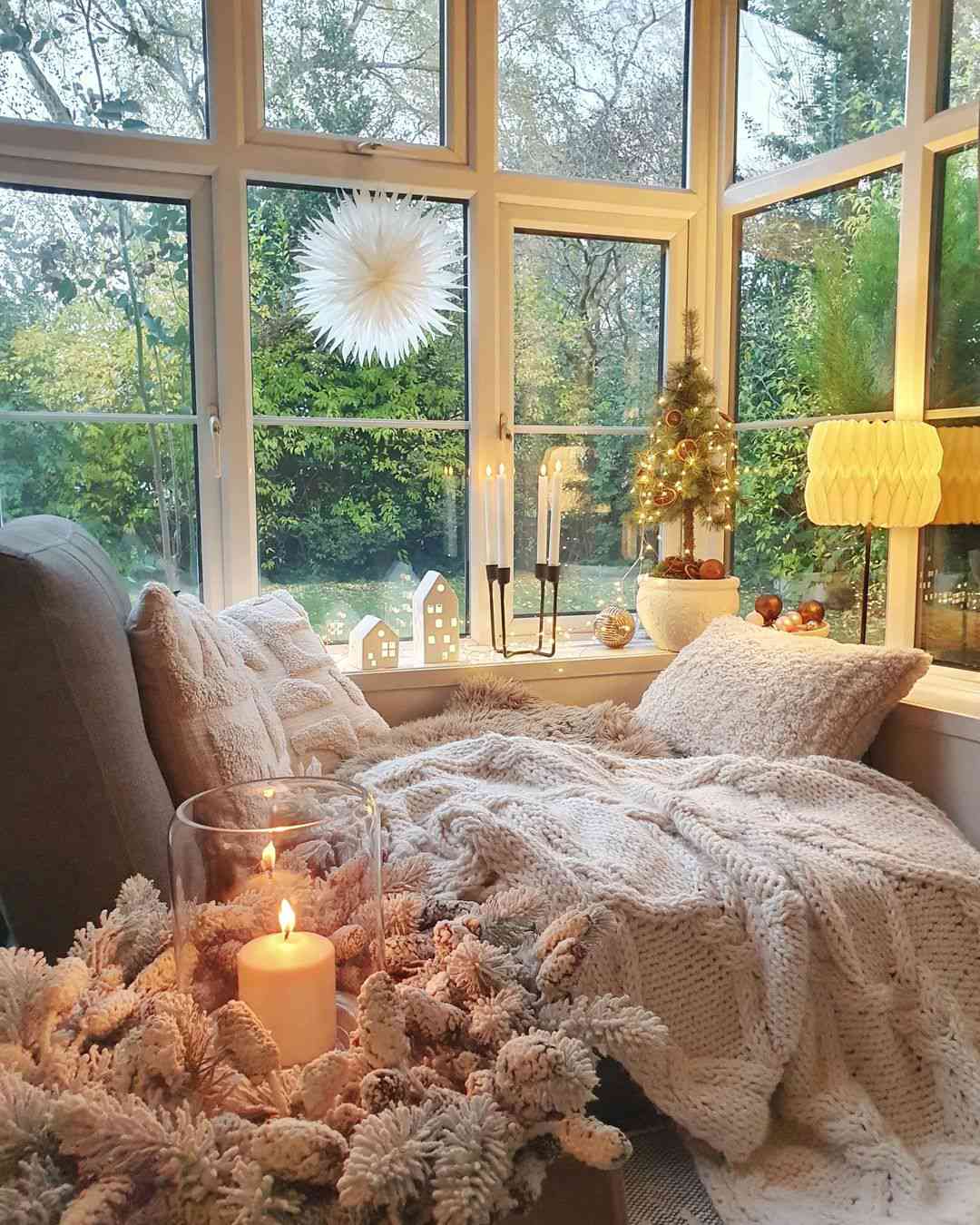 Decorations and lights displayed on the window sill in a sunroom with cozy seating