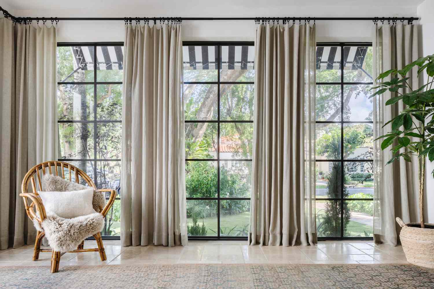 Floor-to-ceiling curtain panels from wall to wall in a sunroom with tiled floors and a rattan armchair in the corner