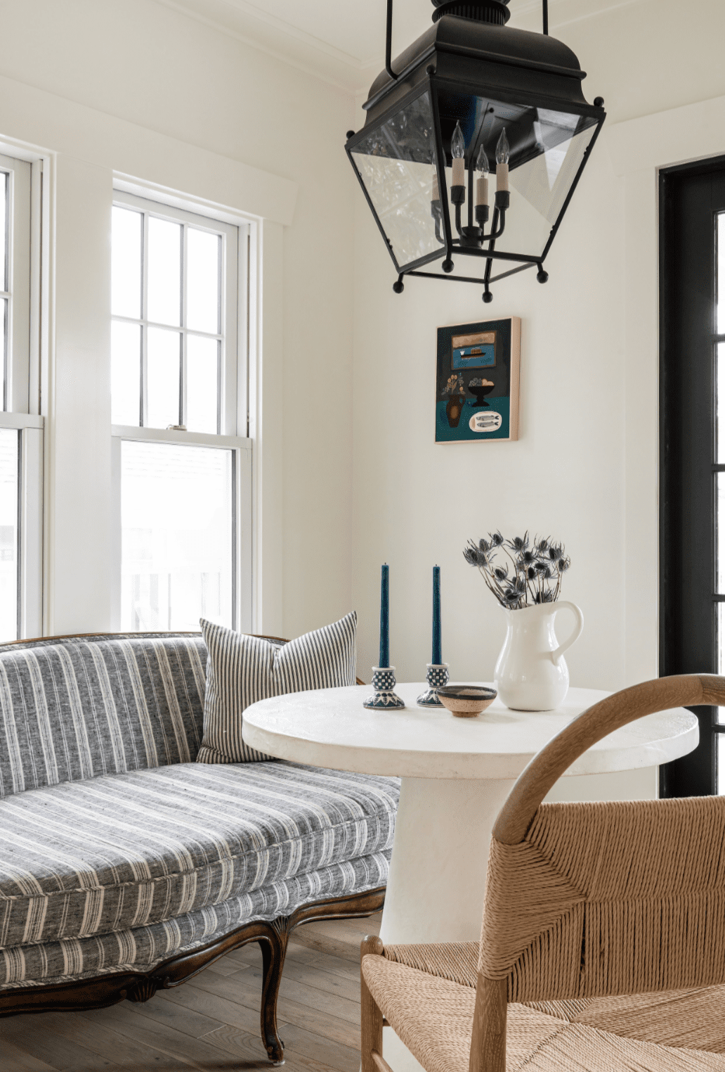 Sunroom breakfast nook with a lantern pendant, upholstered settee, wood chair and modern round table