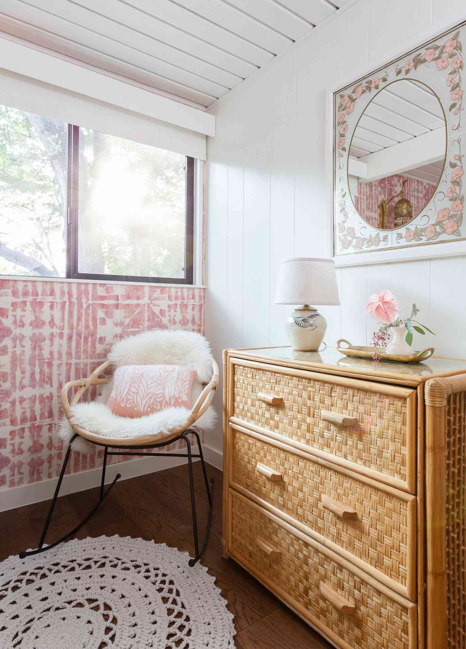 Pink and white decor in a white sunroom with a rattan dresser