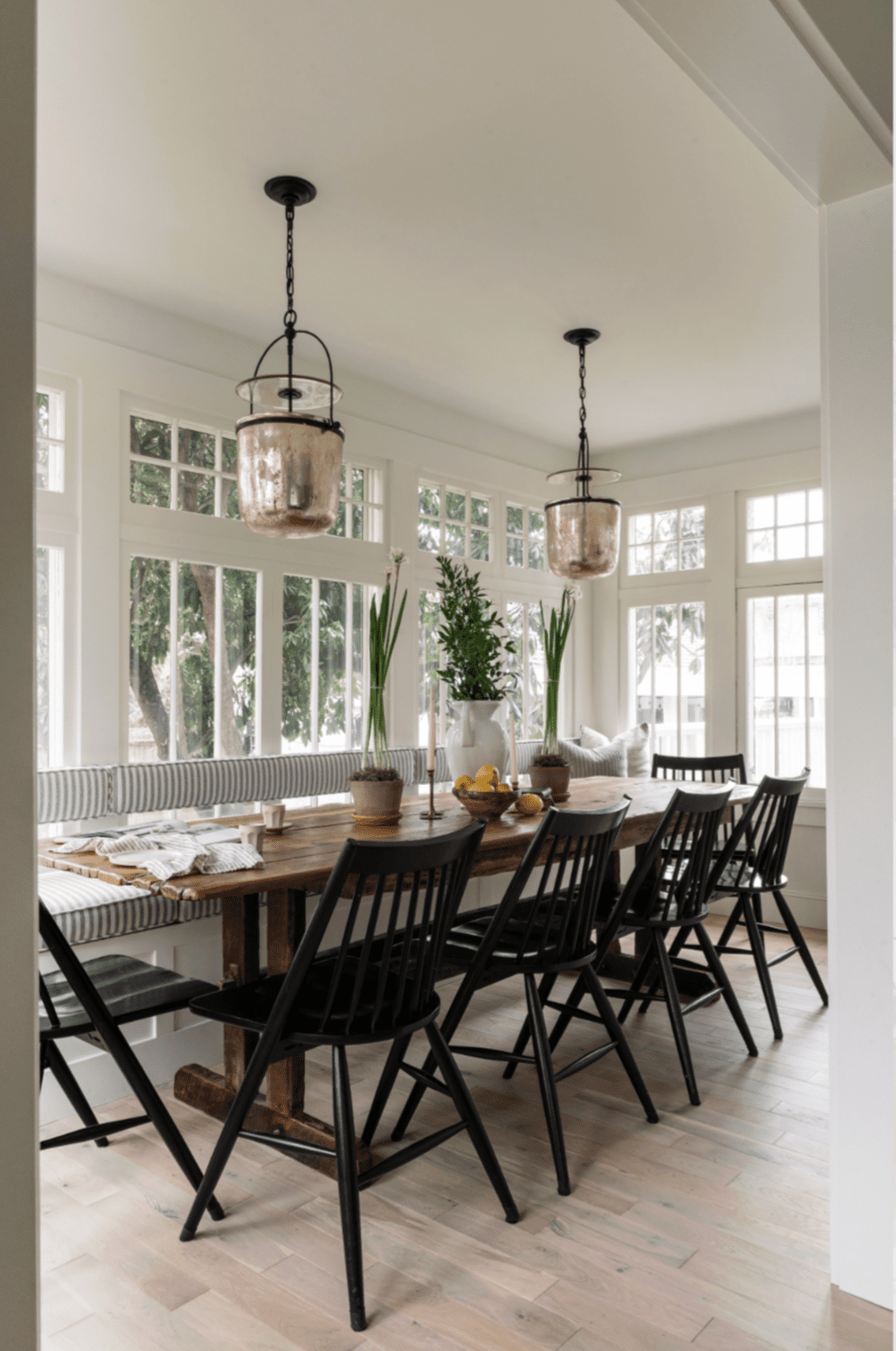 Sunroom used as an elegant dining room with a long table and two pendant lights